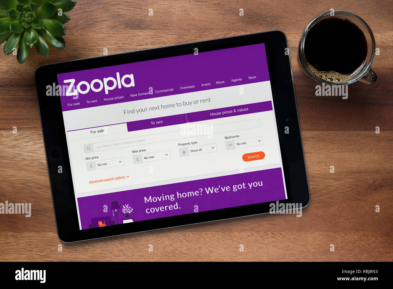 Il sito web di Zoopla è visto su un tablet iPad, su di un tavolo di legno lungo con un caffè espresso e una pianta di casa (solo uso editoriale). Foto Stock