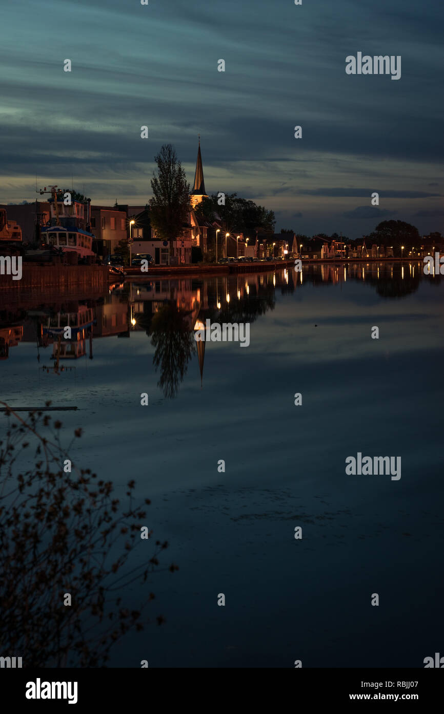 Vista di una città con una chiesa nei pressi di Gouda, Olanda al blue ora. Belle riflessioni di un moody sky. Foto Stock