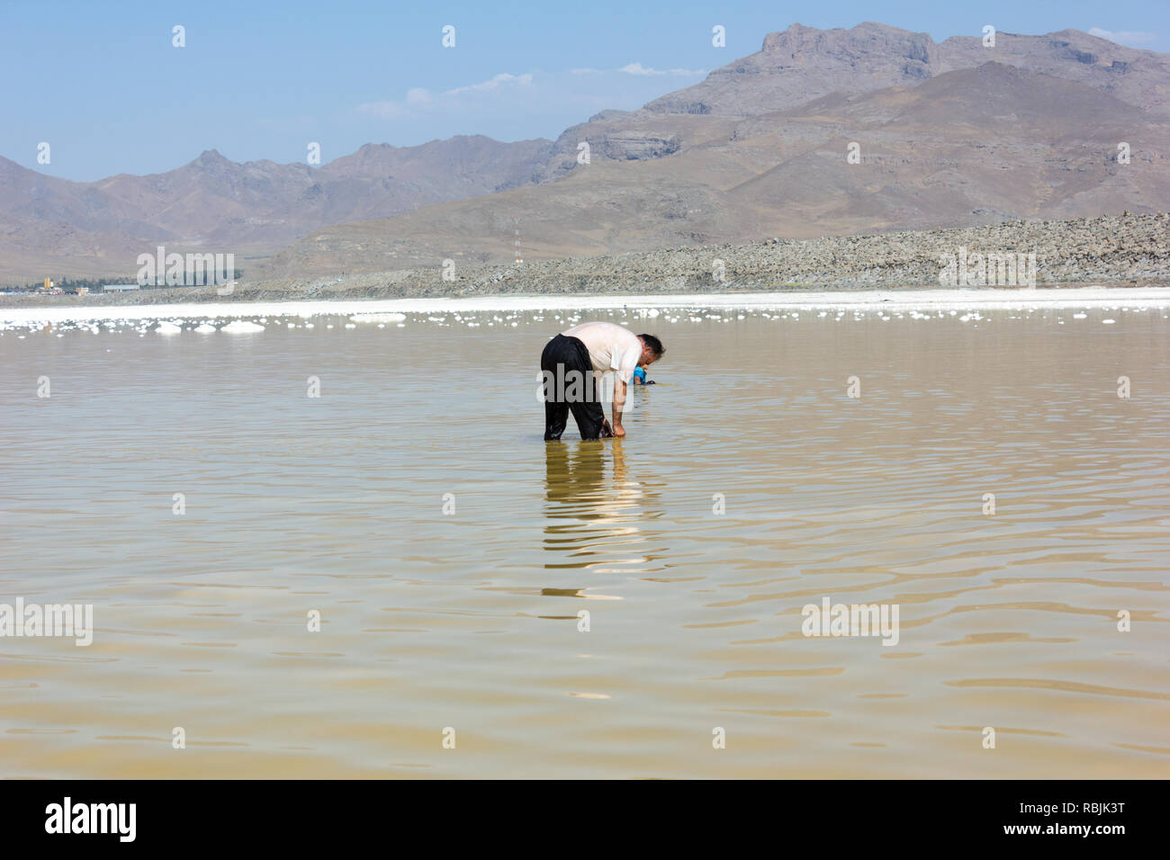 L'uomo in acque poco profonde di Salt Lake Urmia è il prelievo di sale dal pavimento del lago, West Azerbaijan provincia, Iran Foto Stock