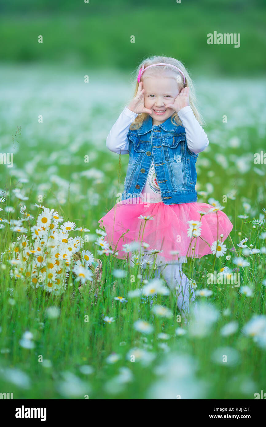 Carino poco sorridente bambina nel campo di camomilla piccolo bambino  biondo con corona sul capo in chamomiles indossano jeans e gonna rosa  godendo nascondi-e-s Foto stock - Alamy