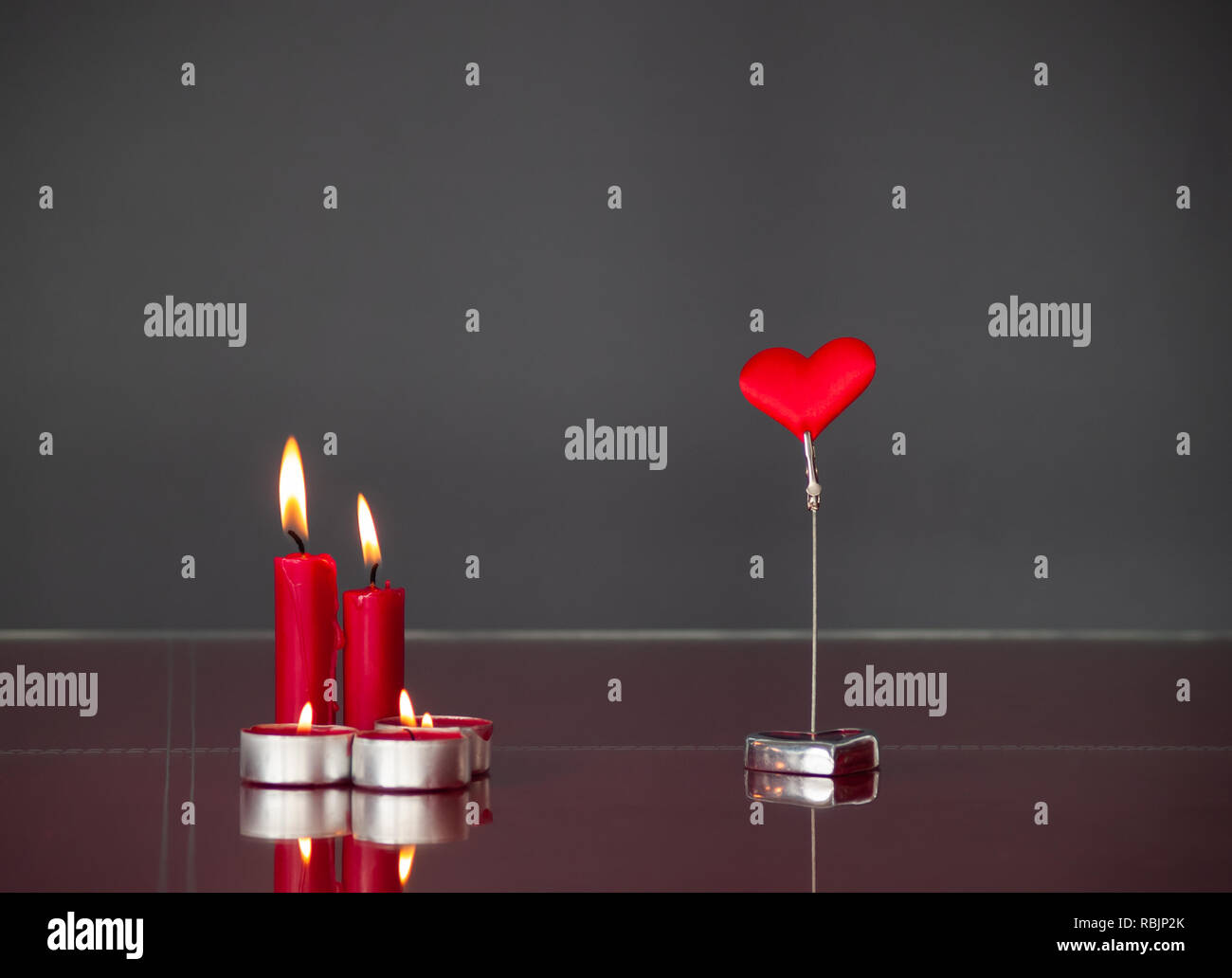 Concetto di amore candele rosse accese e un cuore rosso con sfondo grigio Foto Stock