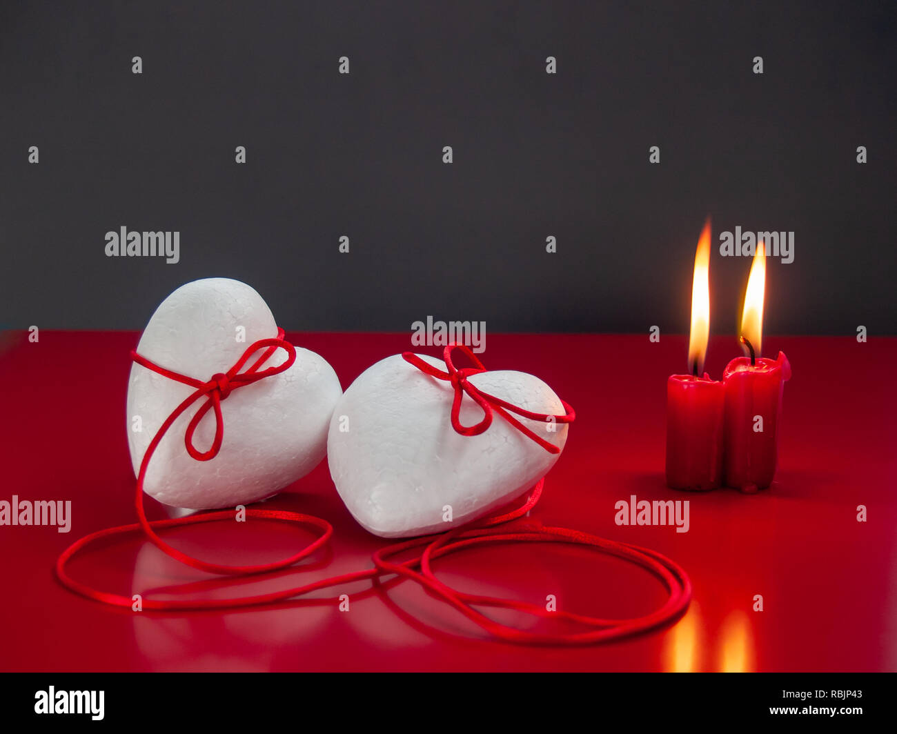 Concetto di amore poliespan due cuori uniti con un filo rosso che simboleggia la leggenda del filo rosso e rosso due candele accese Foto Stock