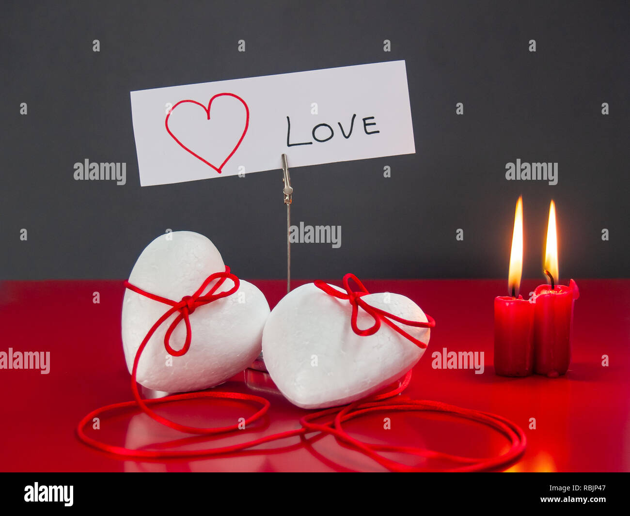 Concetto di amore poliespan due cuori uniti con un filo rosso che simboleggia la leggenda del filo rosso e rosso due candele accese Foto Stock