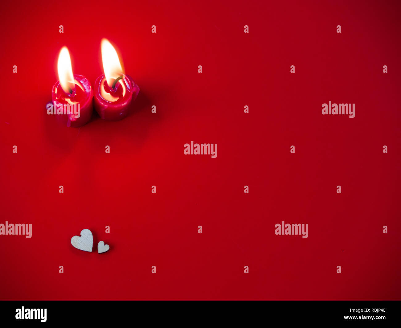 Concetto di amore candele rosse accese e due cuori di legno con uno sfondo rosso Foto Stock