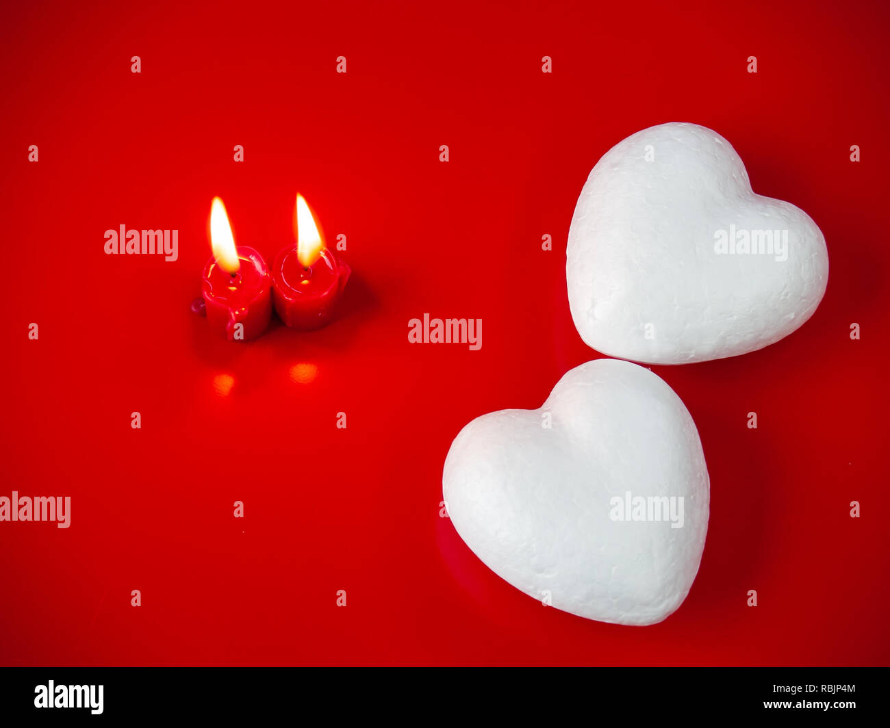 Concetto di amore candele rosse accese e due cuori poliespan con uno sfondo rosso Foto Stock