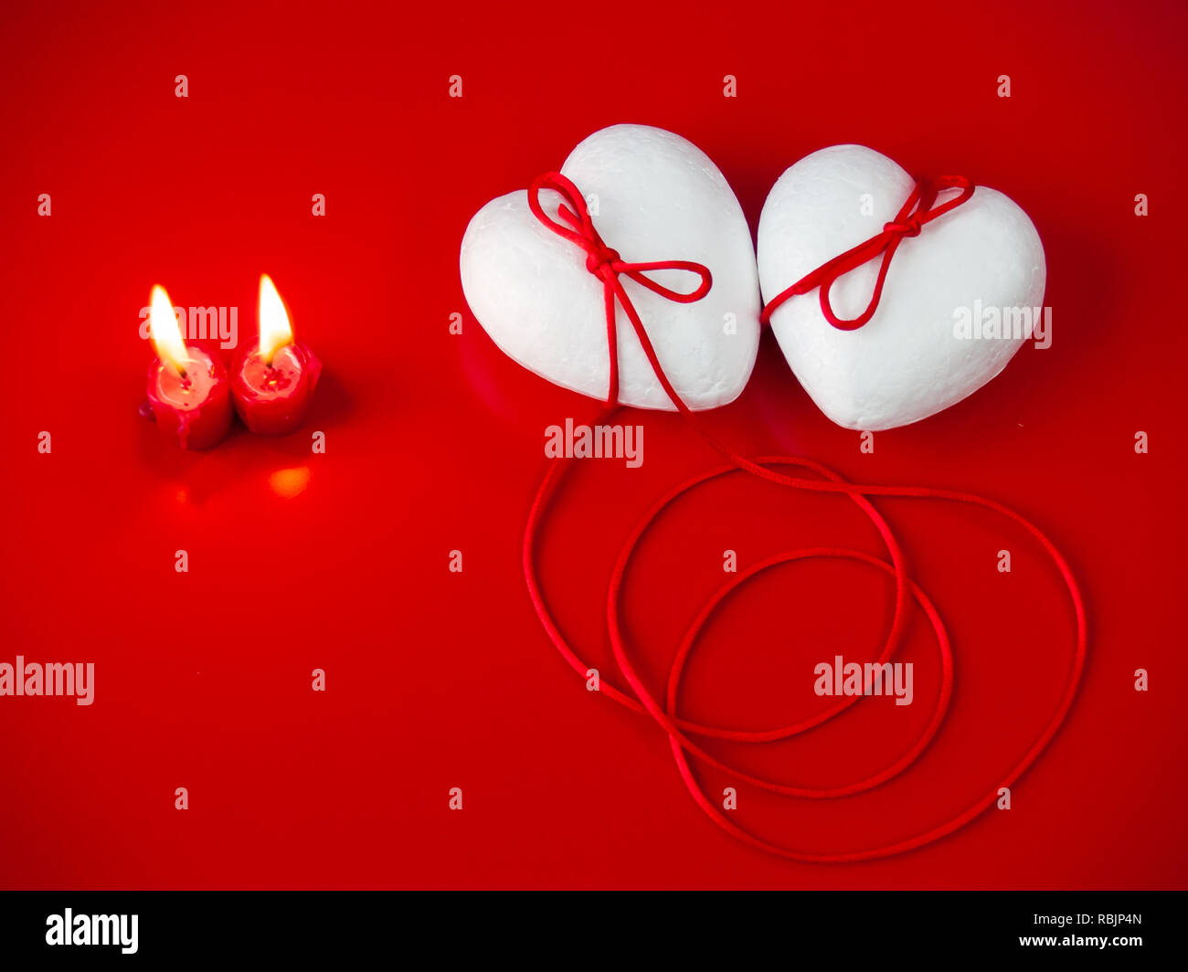 Concetto di amore poliespan due cuori uniti con un filo rosso che simboleggia la leggenda del filo rosso e rosso due candele accese Foto Stock