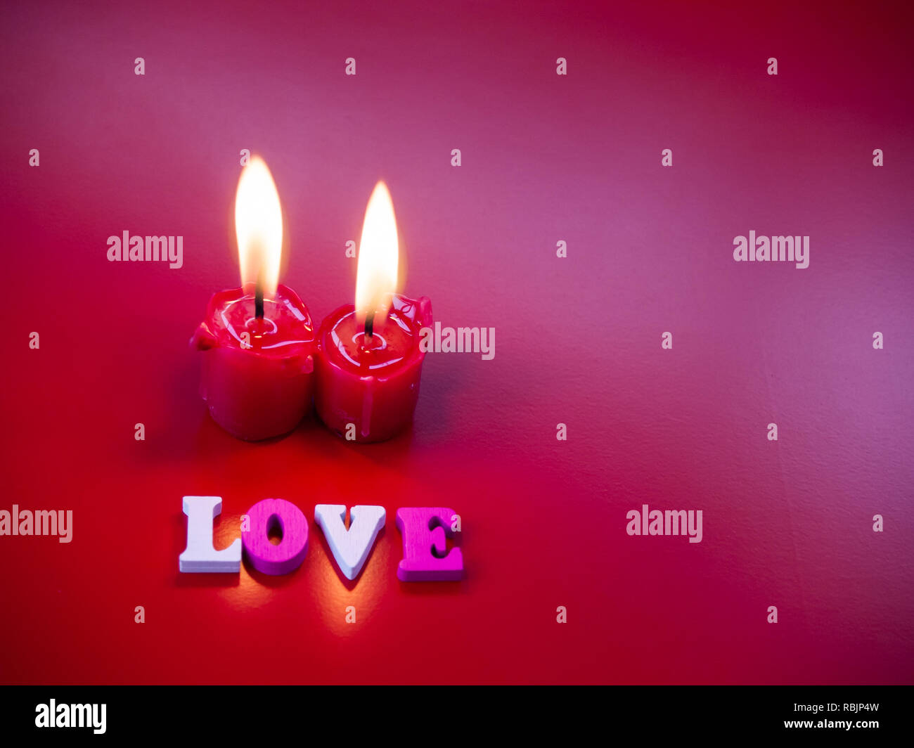 Concetto di amore candele rosse accese e la parola amore con uno sfondo rosso Foto Stock