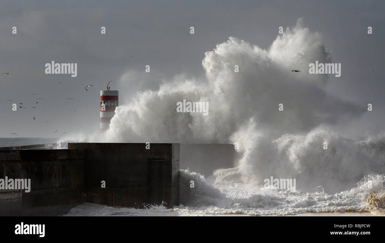 Grande mare tempestoso schizzi d'onda oltre il molo e il faro rotante Foto Stock