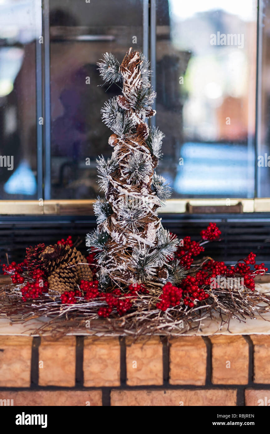 Una decorativa da tavolo piccolo albero di Natale con un anello di bacche rosse impostazione su un mattone camino. Foto Stock