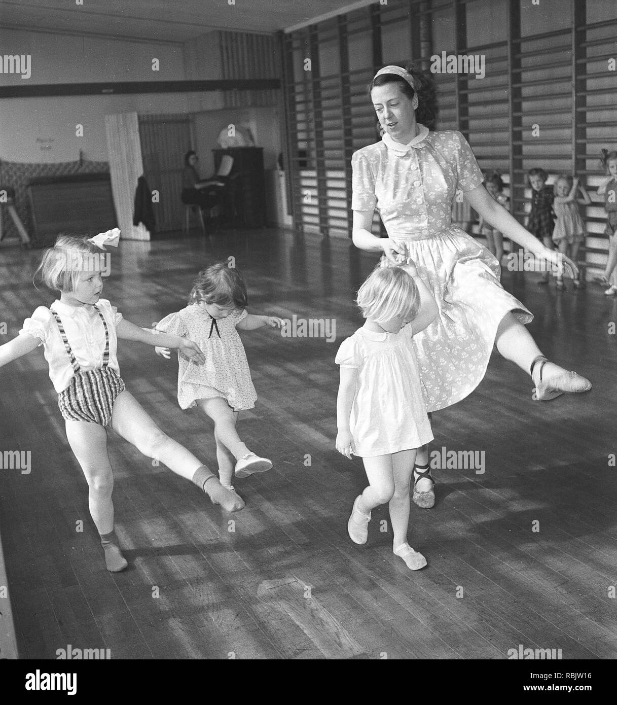 Ginnastica in 1940s. Un insegnante di donne nella palestra della scuola è che mostra come spostare e danza. Tre bambini in età diverse cerca di seguire il suo piombo. Foto Kristoffersson Ref AC3-1. La Svezia 1940s Foto Stock