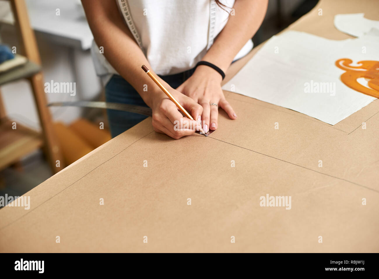 Luogo di lavoro di design studio, creazione di modello di processo. Femmina mani designer close-up rendendo le linee di disegno su cartone utilizzando una matita e il righello. Exclusi Foto Stock