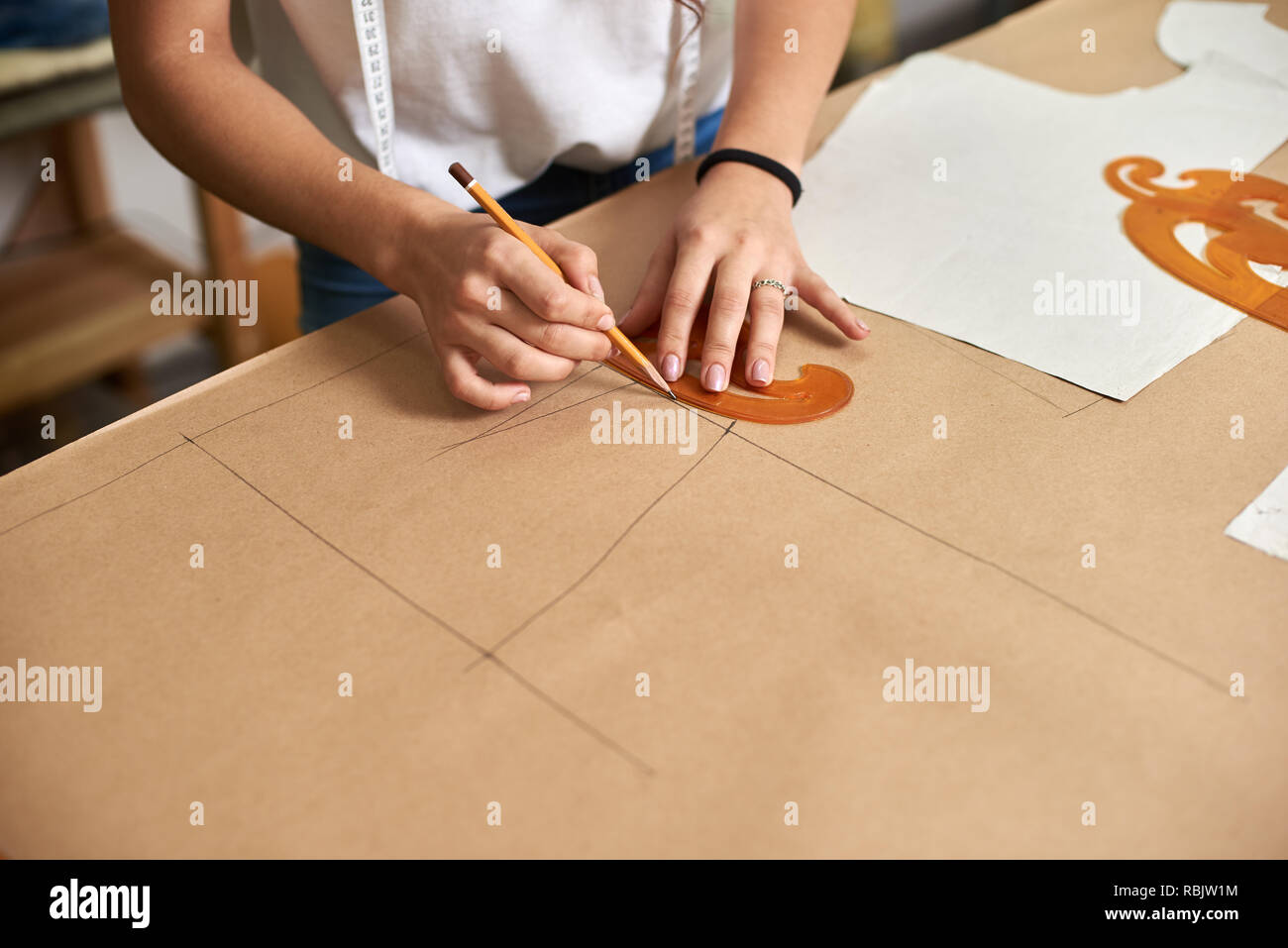 Luogo di lavoro di design studio. Femmina mani designer close-up rendendo il disegno di donna gonna modello dettaglio su cartone utilizzando una matita e curve. Exclusiv Foto Stock