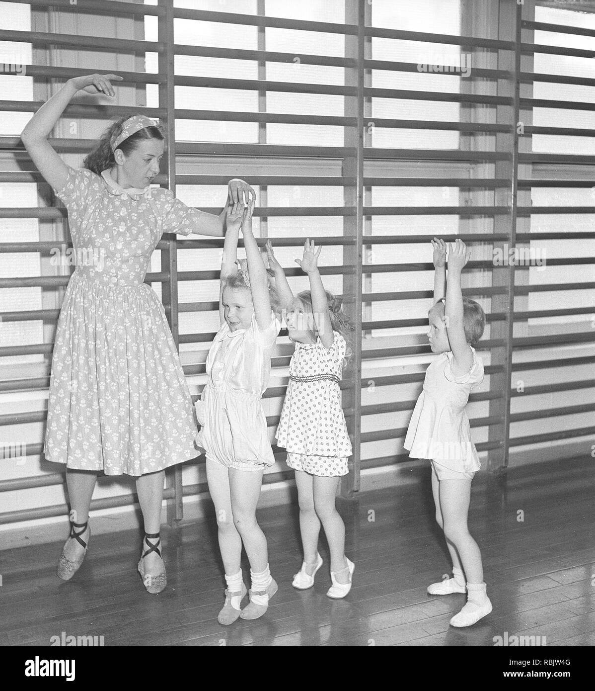 Ginnastica in 1940s. Un insegnante di donne nella palestra della scuola è che mostra come spostare e danza. Tre bambini in età diverse cerca di seguire il suo piombo. Foto Kristoffersson Ref AB22-12. La Svezia 1940s Foto Stock