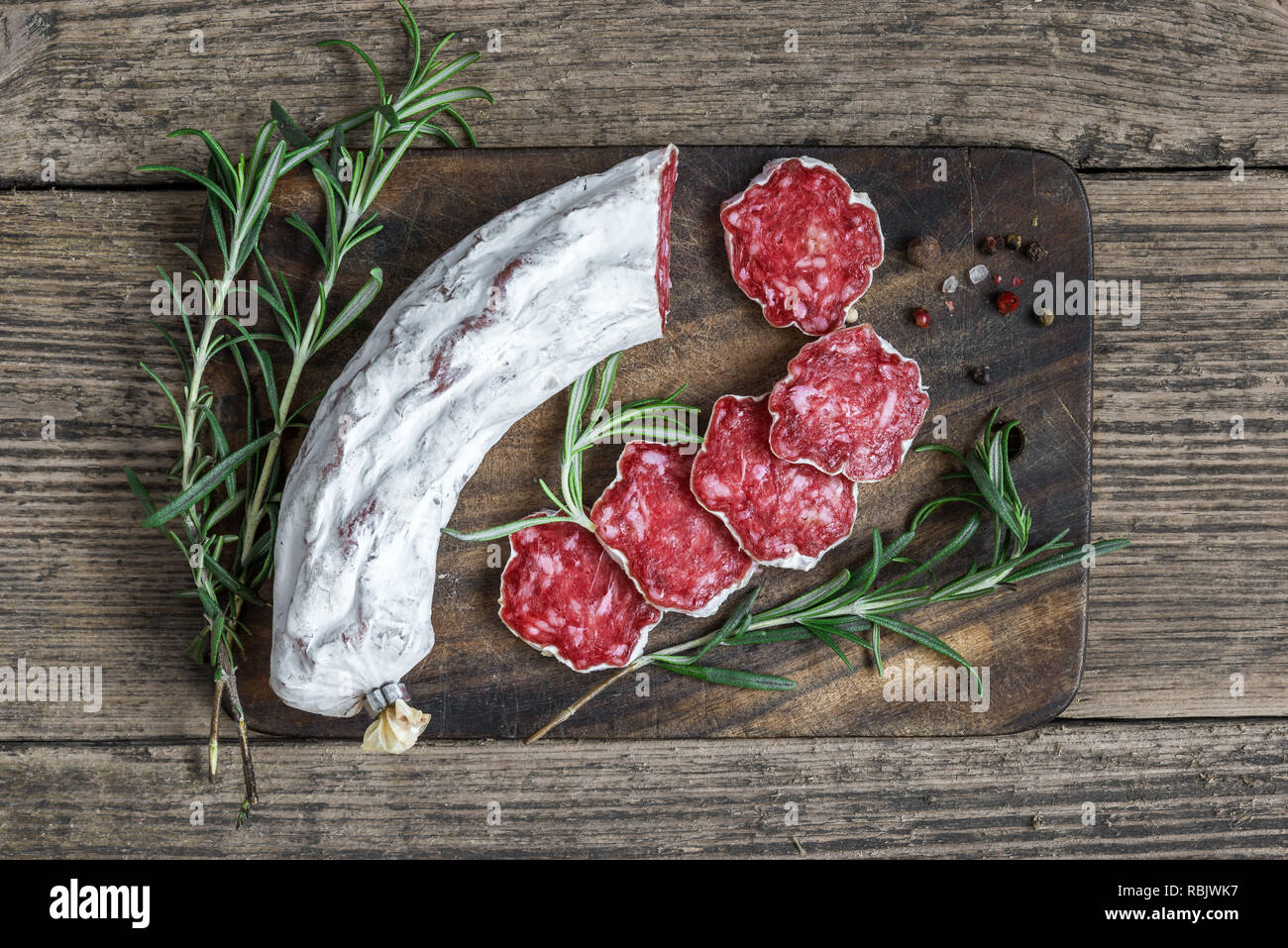 Fette di salame con spezie e rosmarino sul tagliere di legno su tavolo rustico. vista superiore Foto Stock