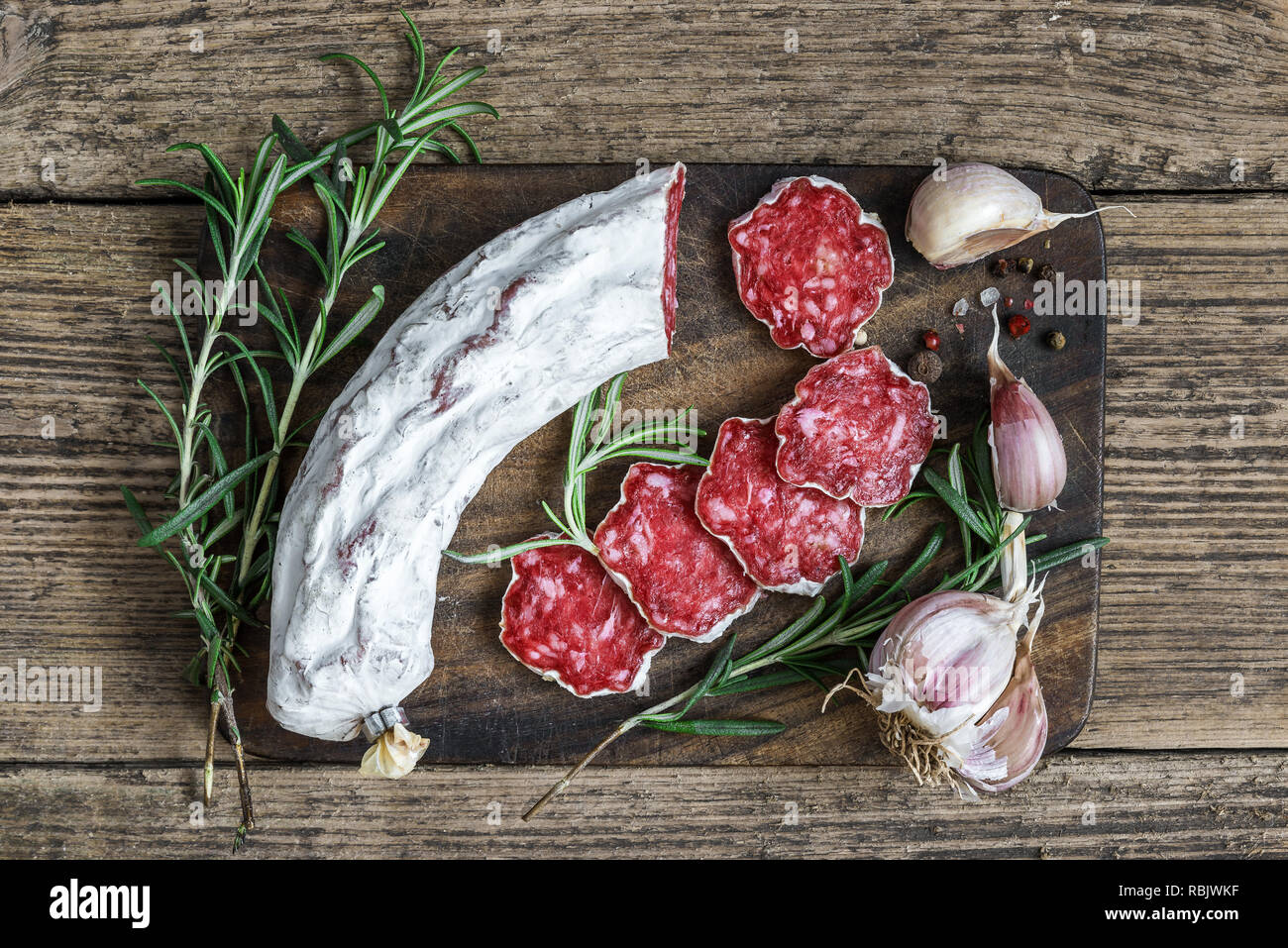 Salame francese con rosmarino, aglio e pepe in grani sul tagliere di legno su sfondo rustico. vista superiore. laici piatta Foto Stock