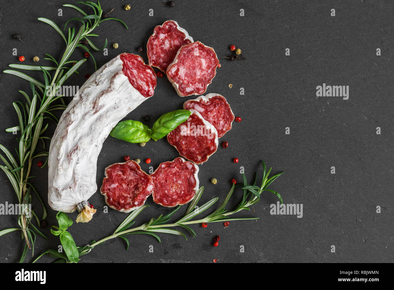 Salame tirata la salsiccia con rosmarino e pepe nero su sfondo di ardesia. vista superiore con copia spazio. laici piatta Foto Stock
