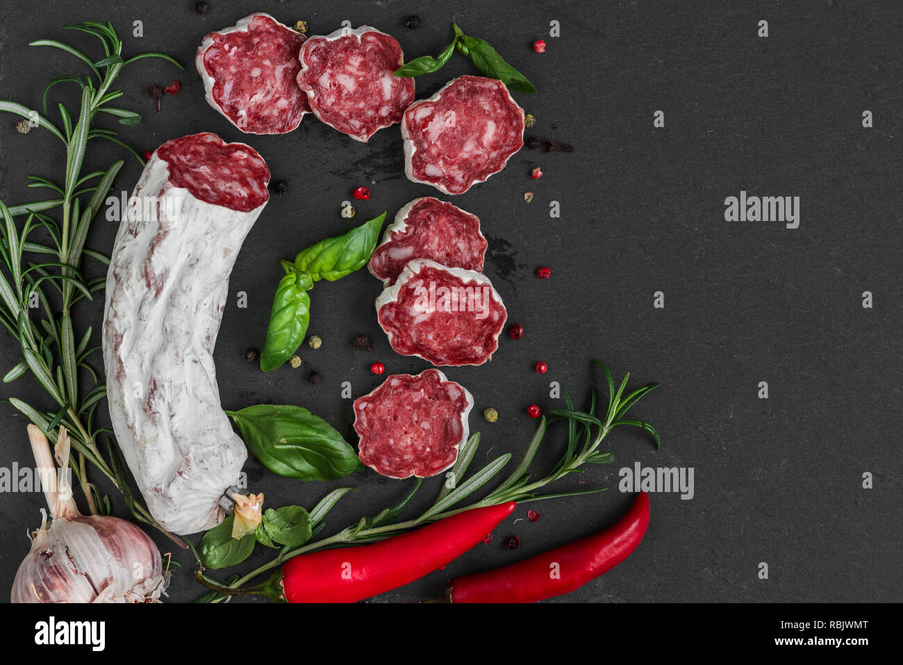 Salame francese con rosmarino, aglio, peperoncino e pepe nero su sfondo di ardesia. vista superiore con copia spazio. laici piatta Foto Stock