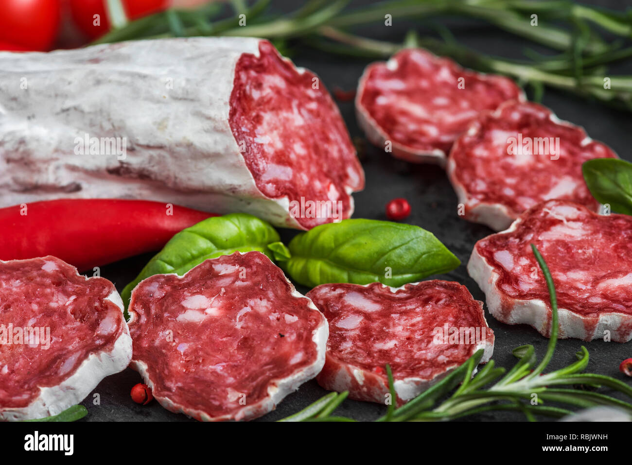 Salame francese con rosmarino, aglio, peperoncino e pepe nero su sfondo di ardesia. close up Foto Stock