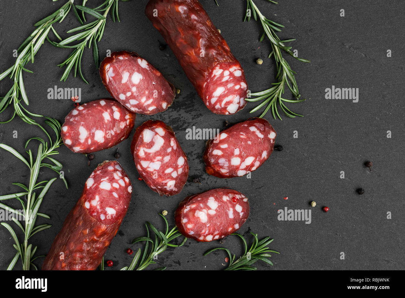 Salame affumicato su nero ardesia sfondo. Salsicce con rosmarino e pepe. vista superiore con spazio di copia Foto Stock