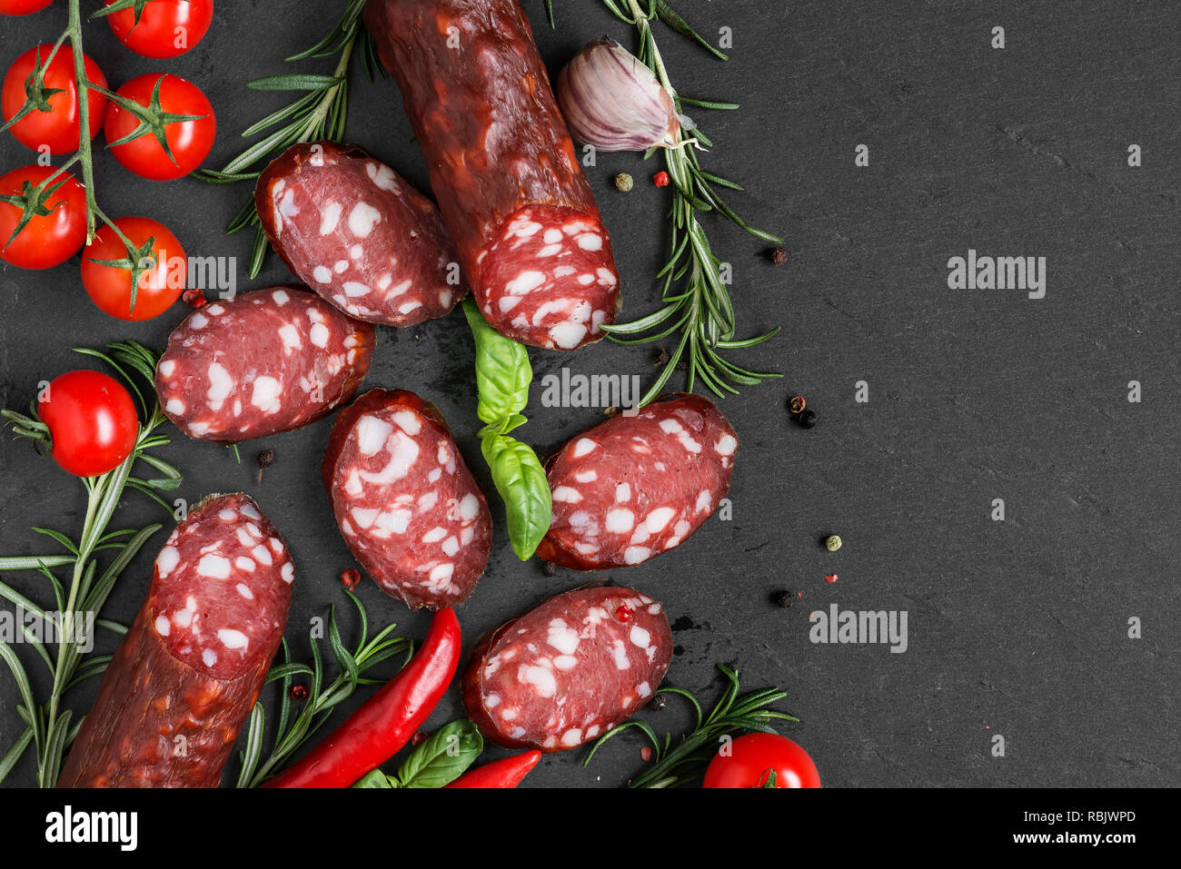 Salume affettato con pomodori, rosmarino e pepe nero su sfondo di ardesia. Insaccato. vista superiore con spazio di copia Foto Stock