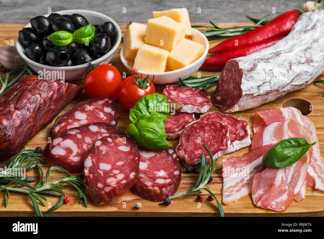 Salame di pancetta affettata, salsiccia, formaggio, olive, pomodori e le erbe aromatiche. Carne Antipasto piatto sul tavolo di legno. close up Foto Stock