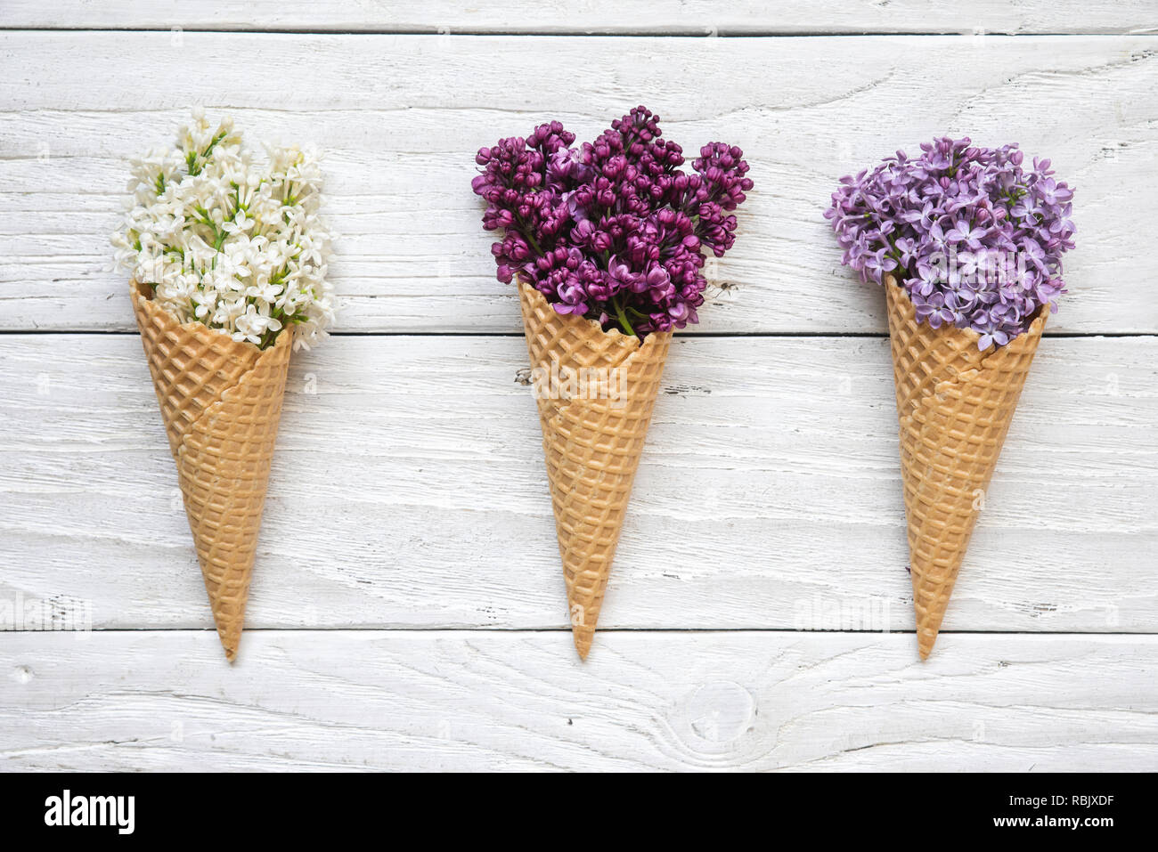 Coni gelato con colorati fiori lilla bianco su sfondo di legno. vista superiore. laici piatta Foto Stock