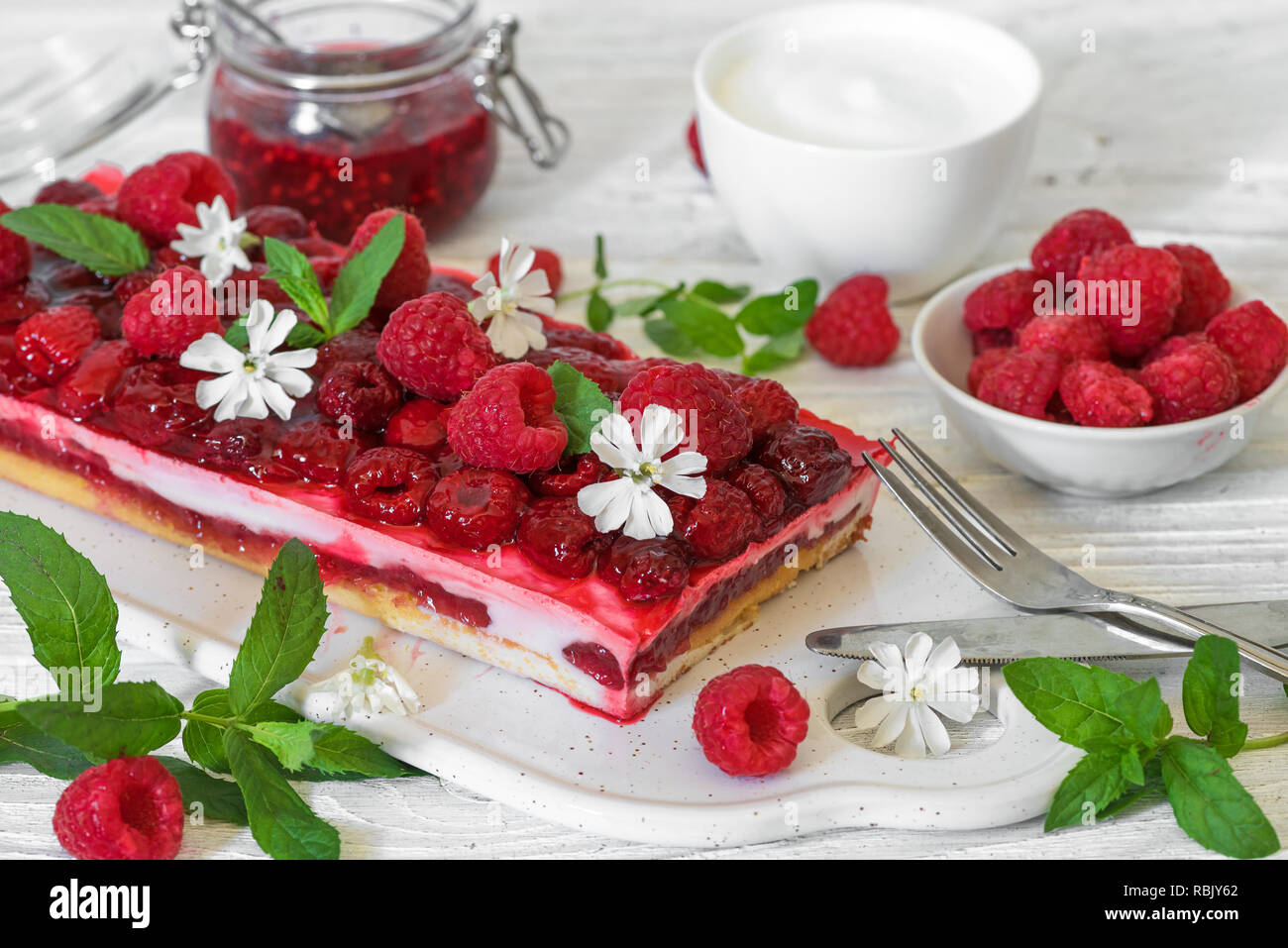 Lampone torta con frutti di bosco freschi e menta decorate con fiori di colore bianco su un tavolo di legno. dessert per colazione. close up Foto Stock