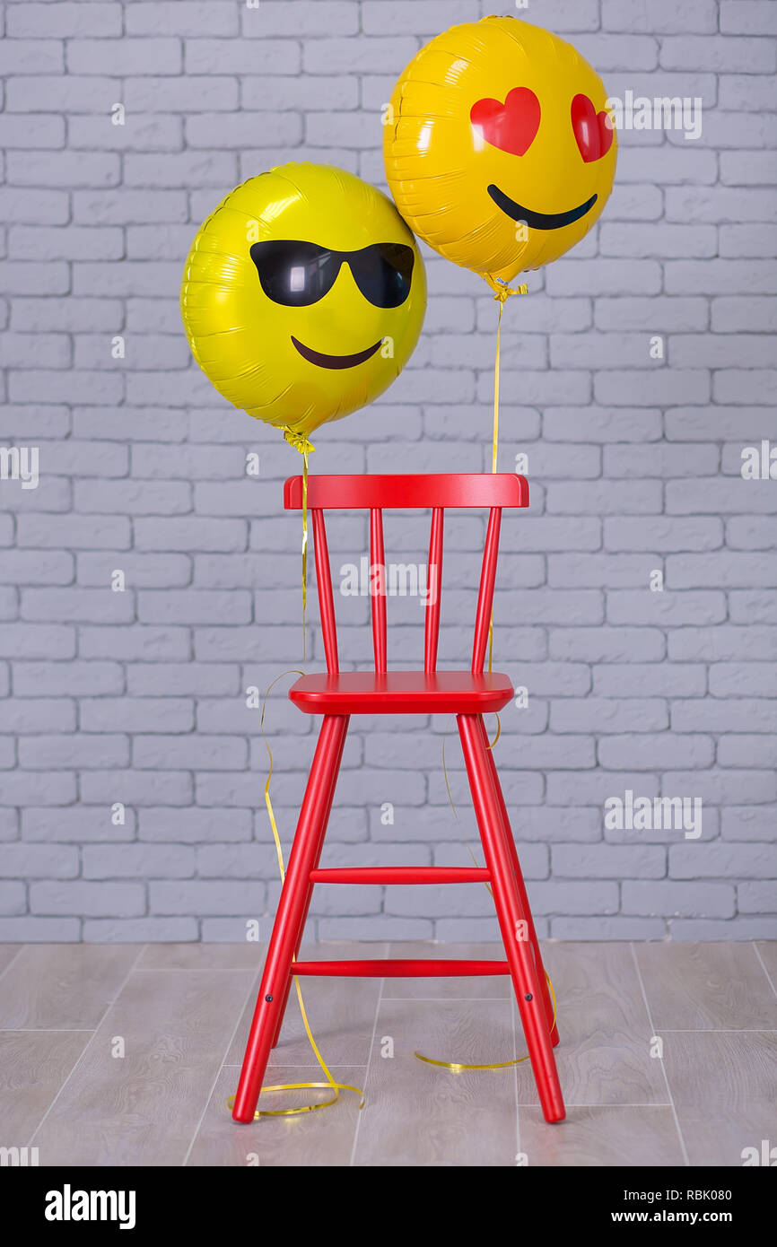 Grigio appartamento studio con sedia, un muro di mattoni, giallo palloncini  dettagli emoji sedia rossa Foto stock - Alamy
