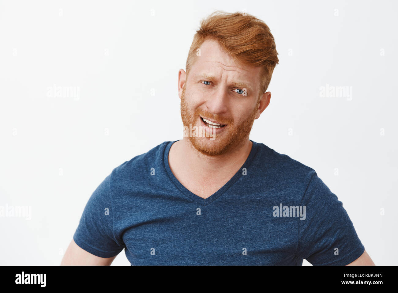 Niente di speciale che posso fare di meglio. Ritratto di dubbio dispiaciuto e deluso bello maschio maturo con i capelli rossi, accigliata e fissando la telecamera, esprimendo antipatia o esitazioni sul muro grigio Foto Stock