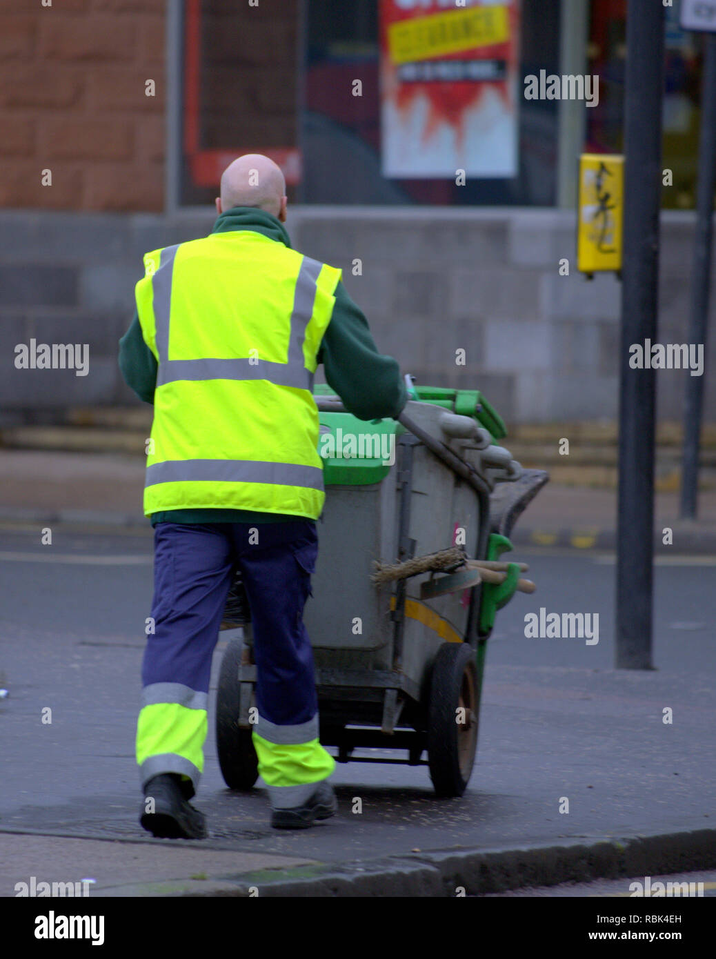 Dustman street sweeper attraversamento strada spingendo il carrello di polvere con spazzole Foto Stock