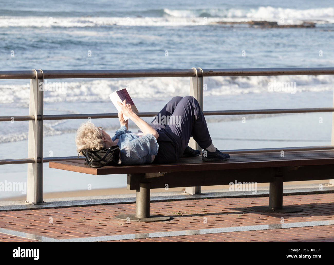 Donna matura la lettura prenota affacciato sulla spiaggia. Foto Stock