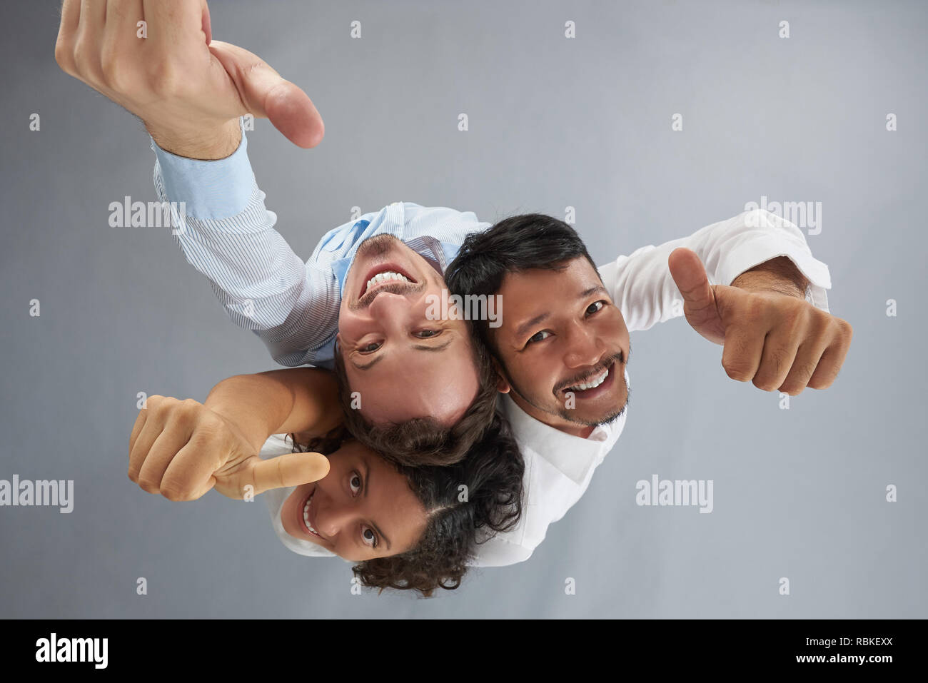 Gruppo di gente sorridente che mostra il pollice al di sopra vista dall'alto su grigio di sfondo per studio Foto Stock