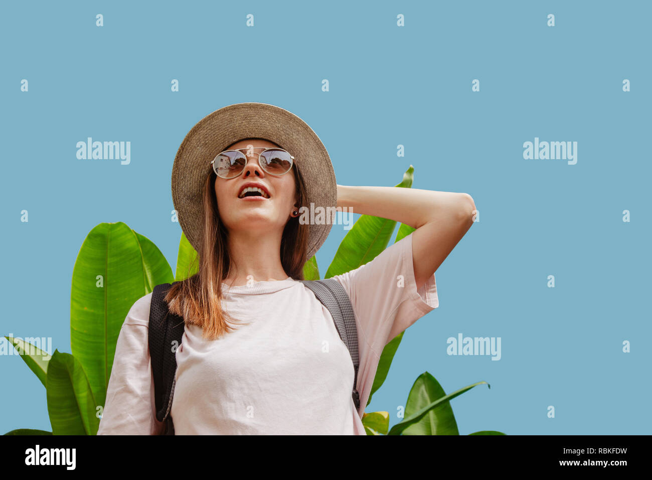 Stupiti donna vicino a pianta tropicale che guarda lontano Foto Stock