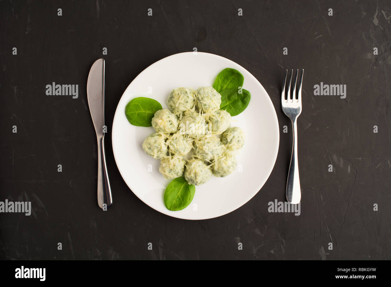 Piastra bianca di gnocchi con spinaci e formaggio con coltello e forchetta su sfondo grigio, piatto laico, vista aerea Foto Stock