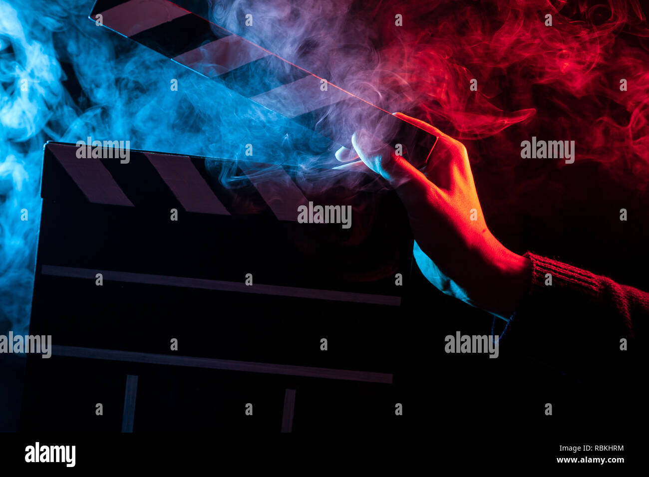 Close-up su un clapperboard aperto a portata di mano prima di iniziare le riprese di un film con multi-fumo colorato intorno con rosso e retroilluminazione blu su un iso nero Foto Stock