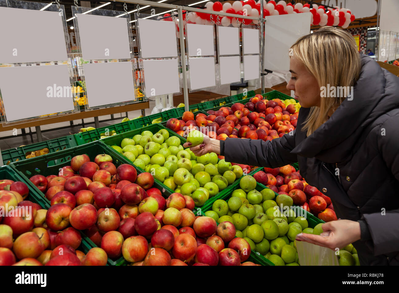 Una donna bionda in un supermercato compra le mele, appoggia attraverso diversi tipi di mele che sono splendidamente esposte sugli scaffali a prendere, arresto Foto Stock