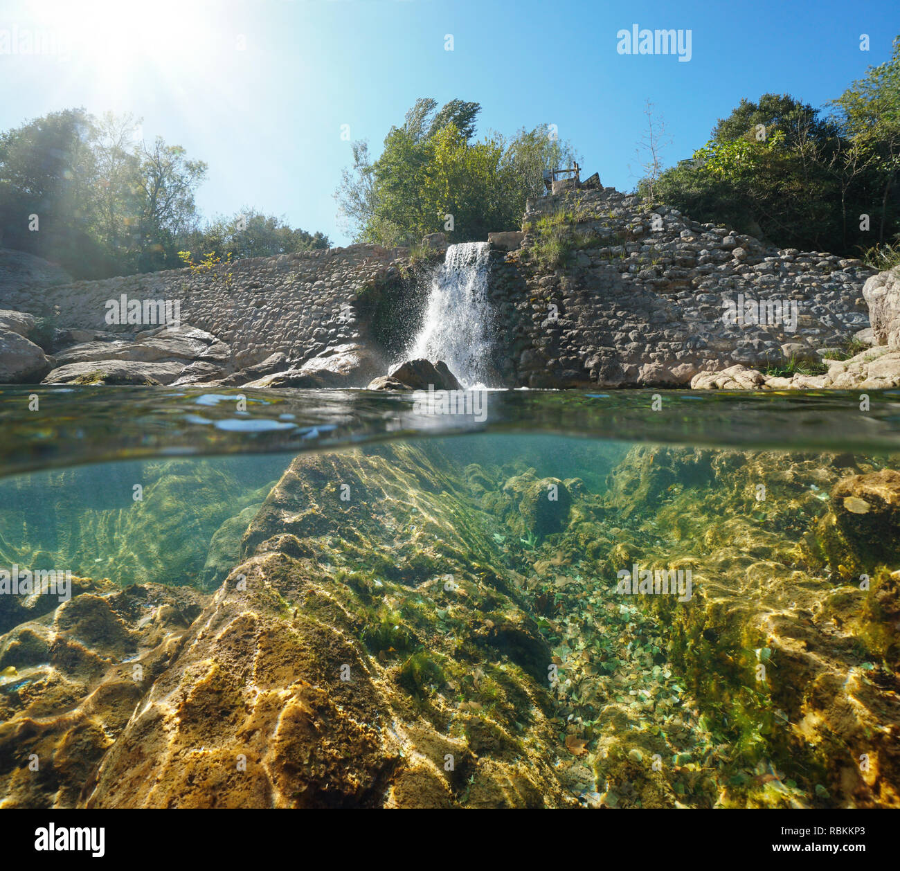 Pietra vecchia diga sul fiume con rocce sottomarine, vista suddivisa per metà al di sopra e al di sotto della superficie dell'acqua, Sant Llorenç de la Muga, Catalogna, Spagna Foto Stock