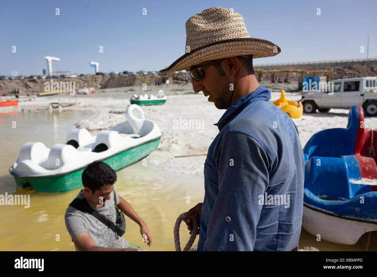 Un giovane uomo in piedi nella spiaggia di sale Urmia Lake e a dare in affitto la barca da diporto, West Azerbaijan provincia, Iran Foto Stock