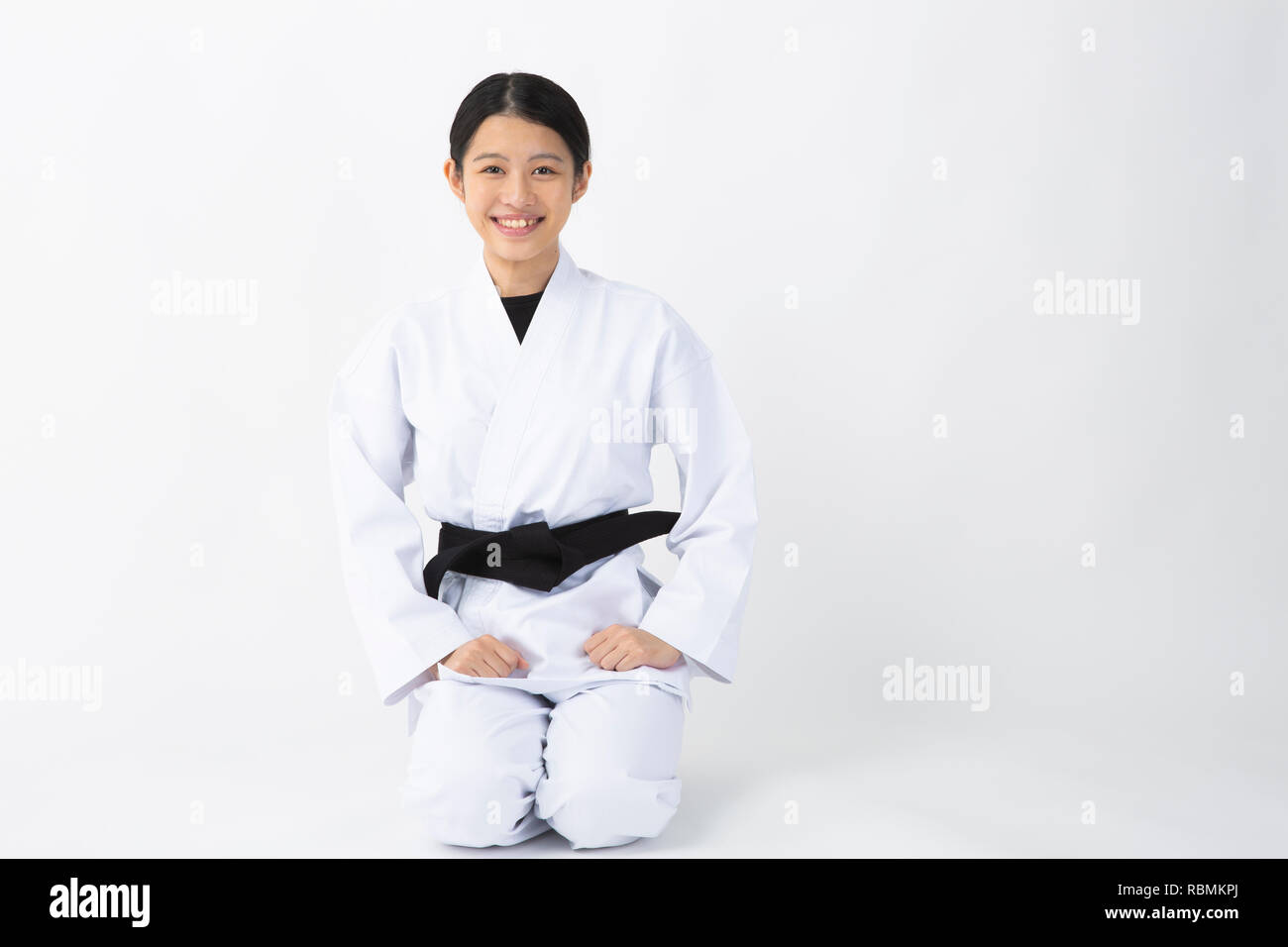 Giovane bella donna che indossa il karate suit seduto e sorridente su sfondo bianco Foto Stock