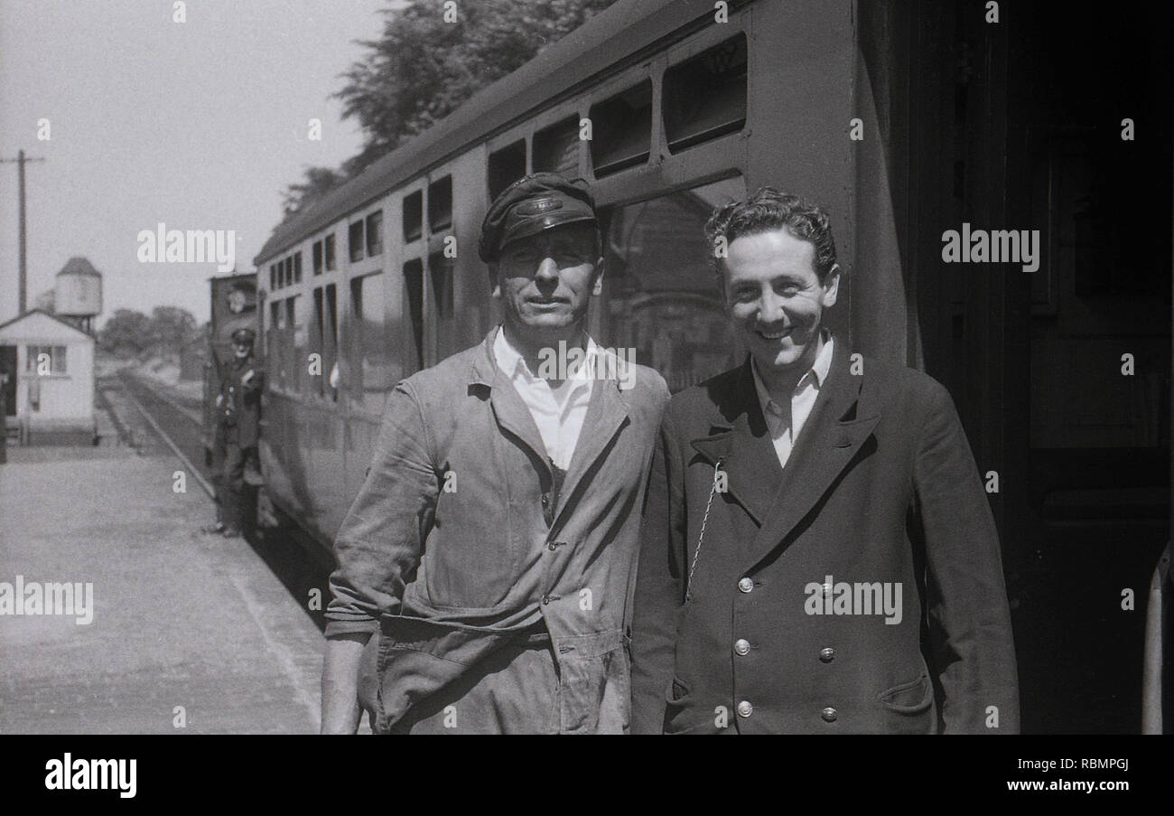 1950, storico, un macchinista in un cappello e una giovane guardia del treno  o conduttore di biglietteria di stare in piedi insieme sulla piattaforma  ferroviaria al di fuori di un carrello per