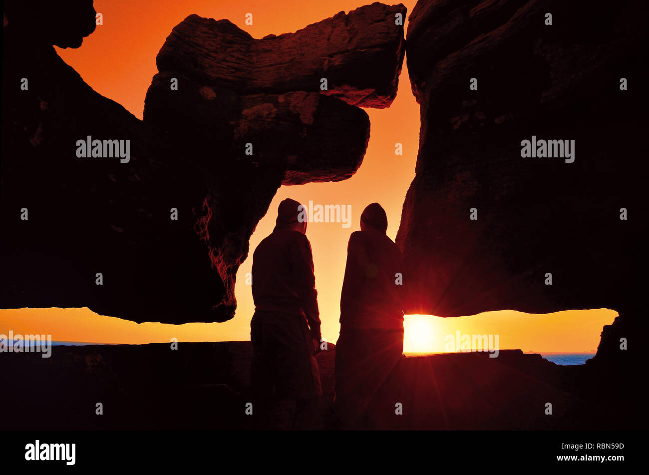 Sagome di due persone a guardare il tramonto ed essendo circondato da formazione di roccia che sembra come una testa del cane Foto Stock