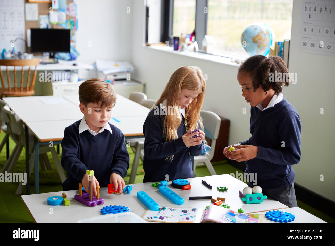 Vista in elevazione dei tre scuola primaria i bambini lavorano insieme utilizzando blocchi di costruzione in una classe Foto Stock