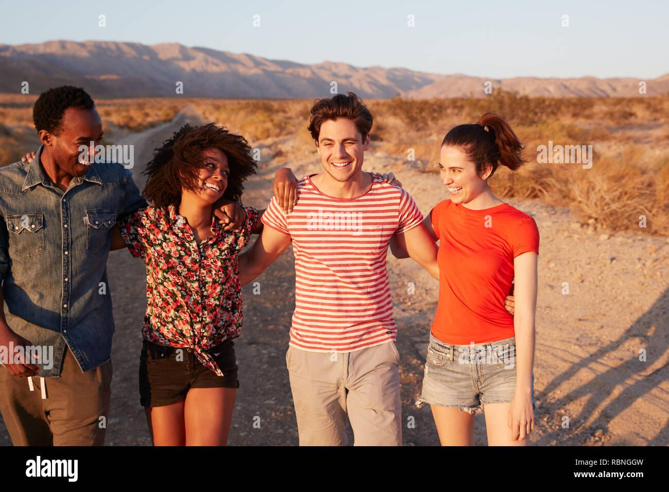 Quattro giovani amici adulti ridere su una strada nel deserto, close up Foto Stock