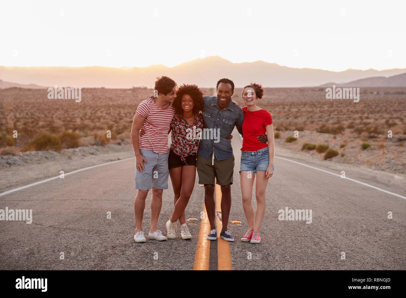 Quattro amici in piedi su un deserto autostrada cercando di fotocamera Foto Stock