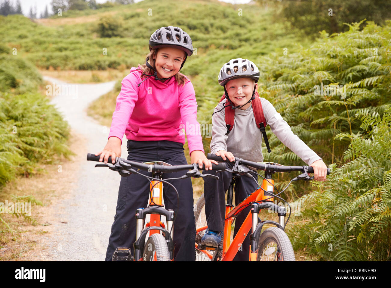 Due bambini seduti sulle loro mountain bike su un percorso di paese a ridere, vista frontale Foto Stock