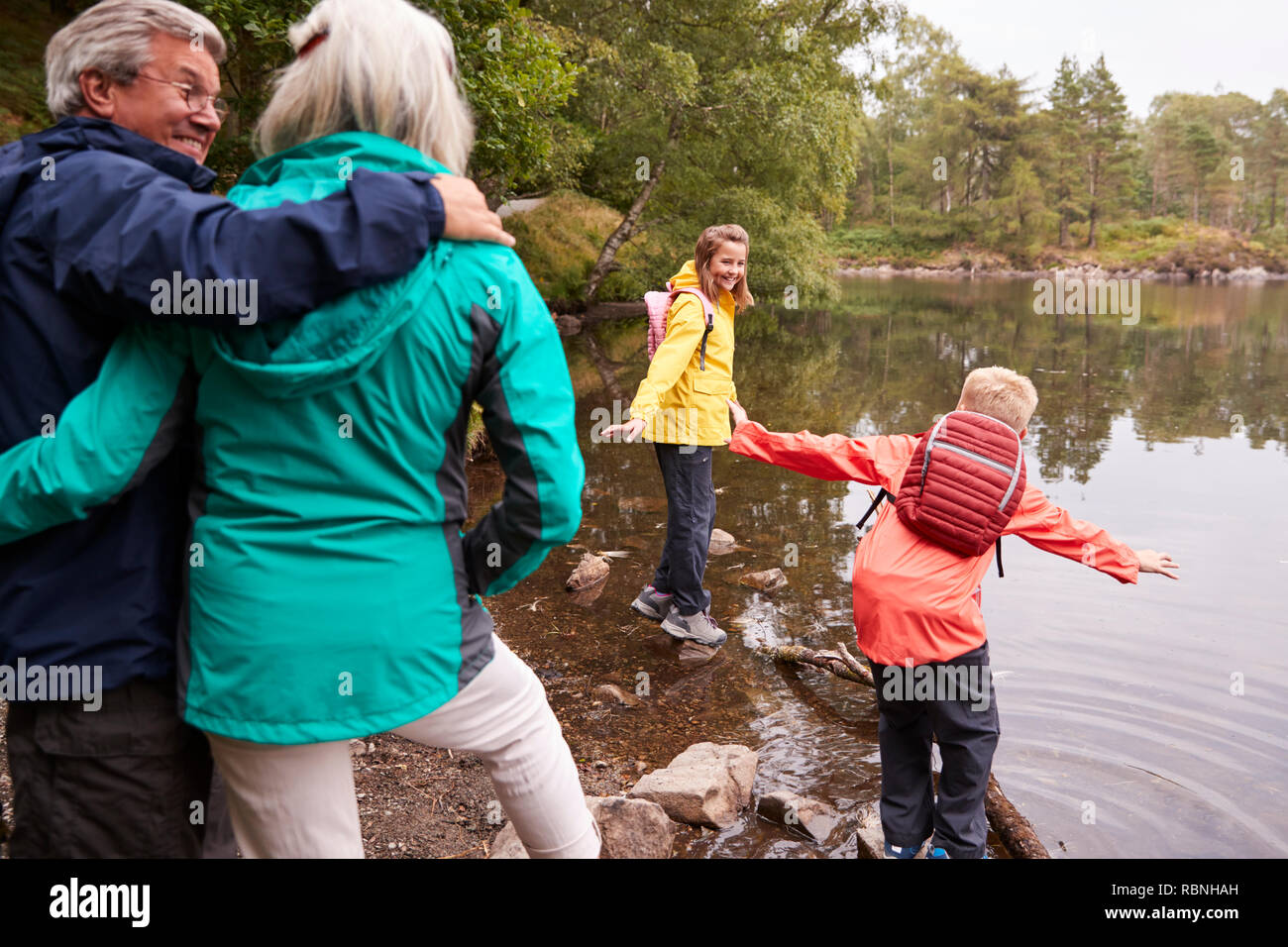 Due bambini che giocano sulla riva di un lago, i loro nonni in primo piano, Lake District, REGNO UNITO Foto Stock