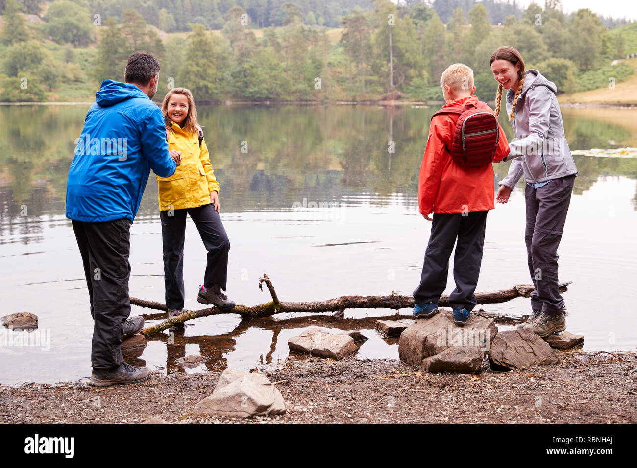 Famiglia giovane giocando con i loro bambini sulle rive di un lago, Lake District, REGNO UNITO Foto Stock