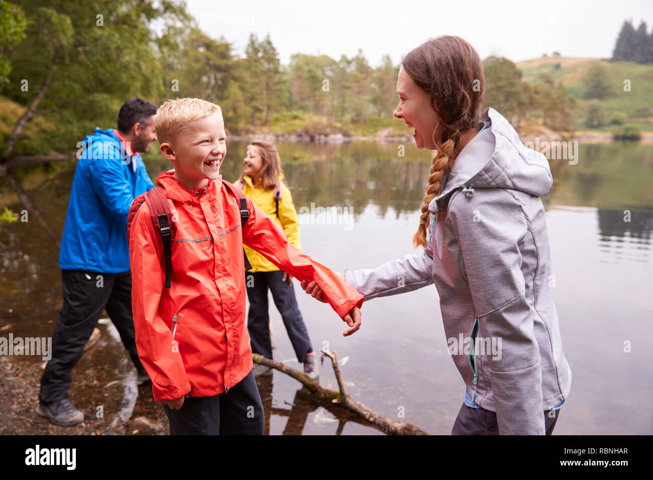 Famiglia giovane giocando con i loro bambini sulle rive di un lago, vicino Lake District, REGNO UNITO Foto Stock