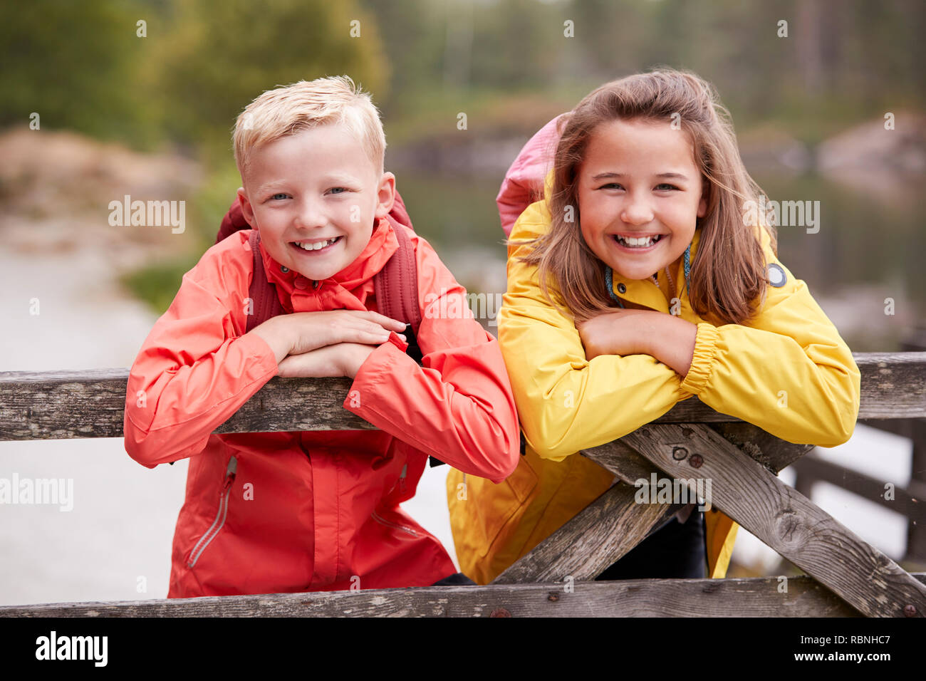 Due bambini appoggiato su di una recinzione di legno nella campagna di sorridere alla telecamera, close up Foto Stock