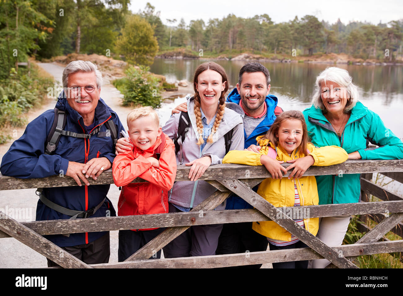 Multi familiare di generazione in piedi dietro una staccionata di legno cercando di fotocamera, Lake District, REGNO UNITO Foto Stock